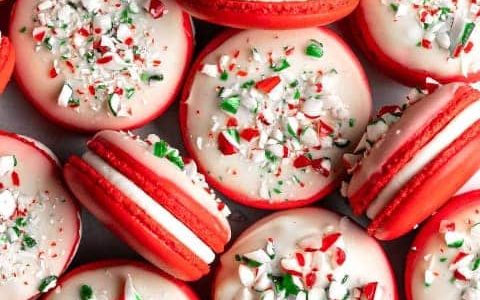 Red macarons filled with mint flavored buttercream and decorated with white chocolate frosting and sprinkles.