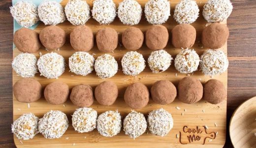Apricot balls wrapped in coconut and cocoa on a wooden cutting board.