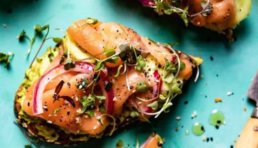 Avocado on a sandwich with salmon and onion.