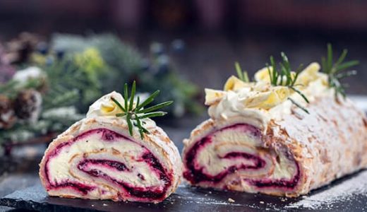 Sliced meringue roll with white chocolate filling and fresh fruit jam decorated with fresh rosemary.