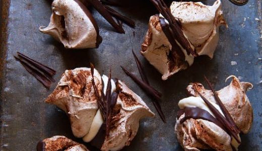 Chocolate meringues with cinnamon glued with apple snow and decorated with chocolate twigs. Next to the meringues is a bowl of apple snow with a knife.
