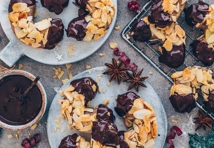 Christmas rolls sprinkled with sliced almonds and dipped in chocolate served on plates.